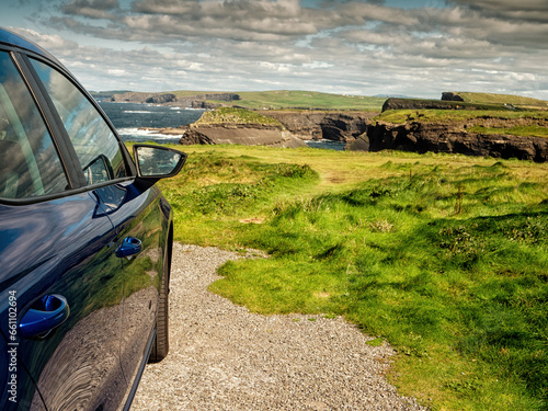 Dark color car parked off road, Stunning nature scene in the background with cliffs and low cloudy sky, sunny day. Kilkee area, Ireland. Travel, tourism and sightseeing concept. Irish landscape. photo