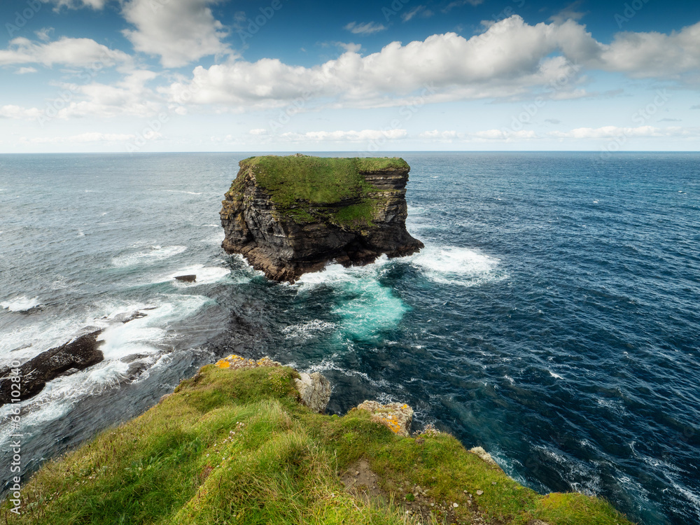 View on rough small island in the ocean from a cliff, Ireland, Kilkee area. Warm sunny day, blue cloudy sky. Travel, tourism and sightseeing concept. Irish landscape and coastline.