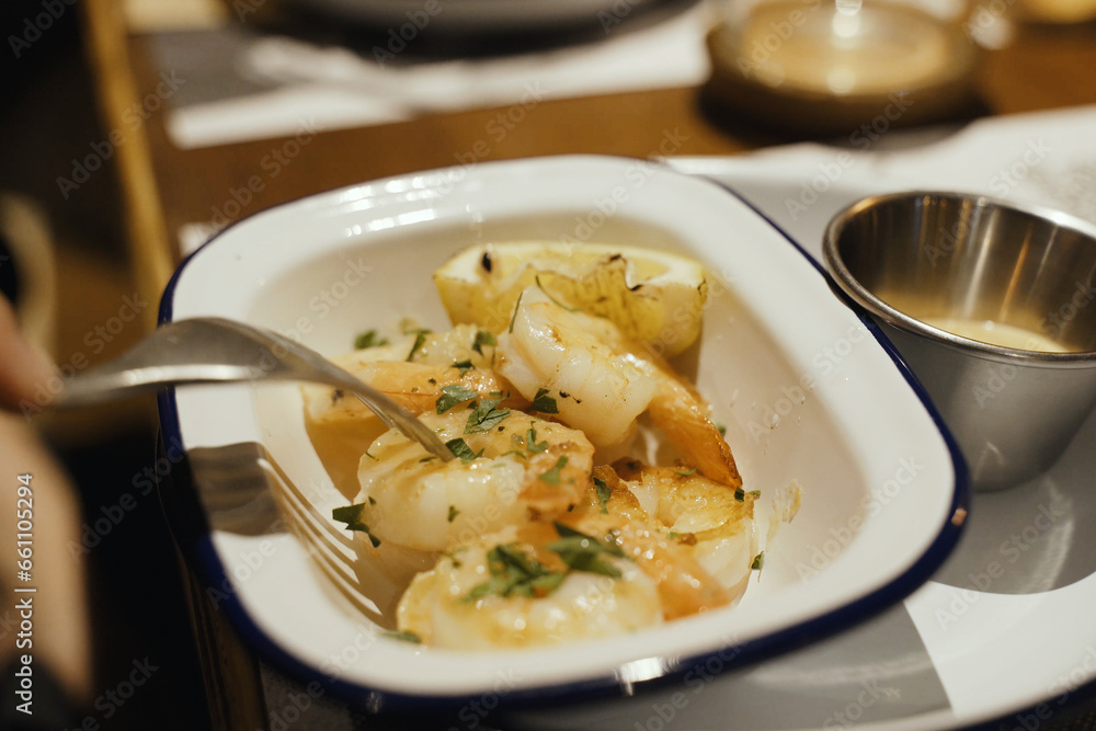 A dish of freshly prepared grilled shrimp with sauce and lemon in a white plate. A dish of freshly prepared grilled shrimp with sauce and lemon in a white plate.