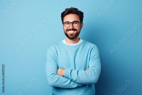 Young handsome man with beard wearing casual sweater and glasses over blue background happy face smiling with crossed arms photo