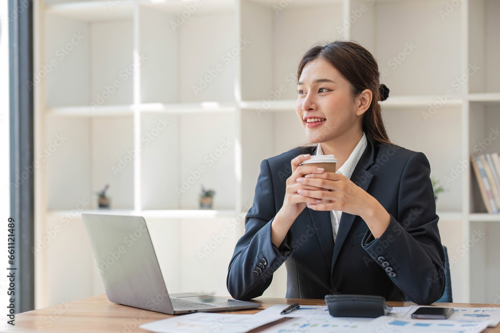 Photo of positive Asian businesswoman holds a cup of coffee imagines plan holiday in office. Photo of positive Asian businesswoman holds a cup of coffee imagines plan holiday in office.