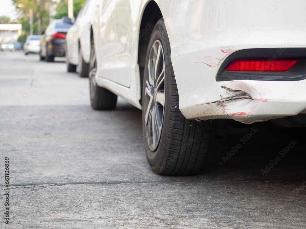 Close up of the rear bumper dent of a white sedan car park on the concrete road