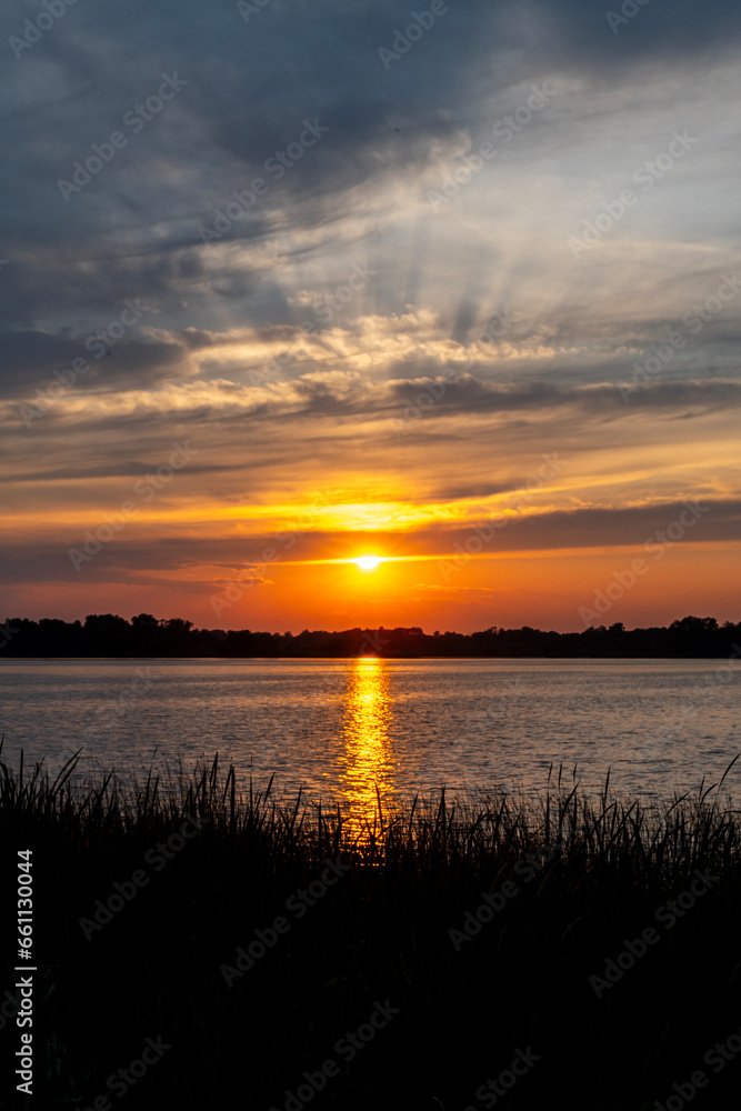 Orange summer sunset  with clouds, God's rays and trees in silhouette at North Turtle Lake in Minnesota, USA
