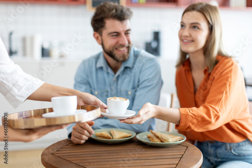 Waiter holding latte on tray, bringing order to man and woman guests, coffeeshop worker give hot drinks to visitors