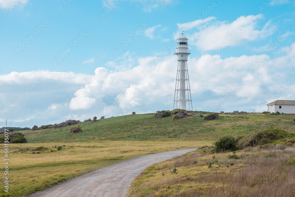 Photograph of a dirt track leading up to Currie Lighthouse on a hill against a cloudy bright blue sky on King Island in the Bass Strait of Tasmania in Australia