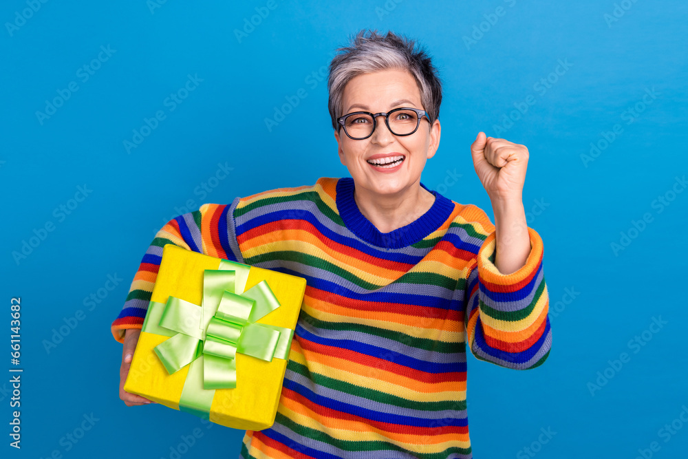 Naklejka premium Portrait of delighted positive person hold desirable giftbox raise fist isolated on blue color background