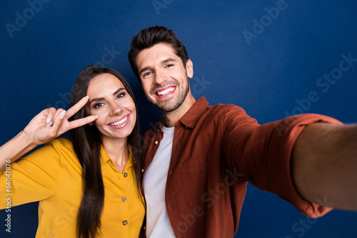 Photo of lovely positive people toothy smile demonstrate v-sign near eye make selfie isolated on blue color background