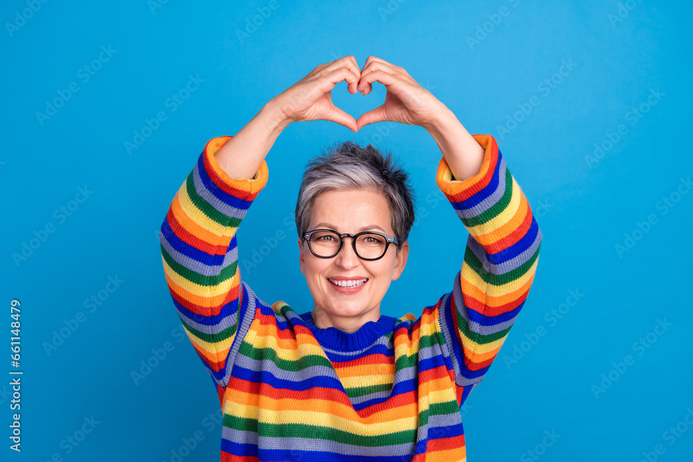 Photo of satisfied positive aged lady toothy smile arms demonstrate heart symbol above head isolated on blue color background Photo of satisfied positive aged lady toothy smile arms demonstrate heart symbol above head isolated on blue color background