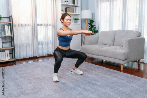 Vigorous energetic woman doing exercise at home. Young athletic asian woman strength and endurance training session as home workout routine with squat.