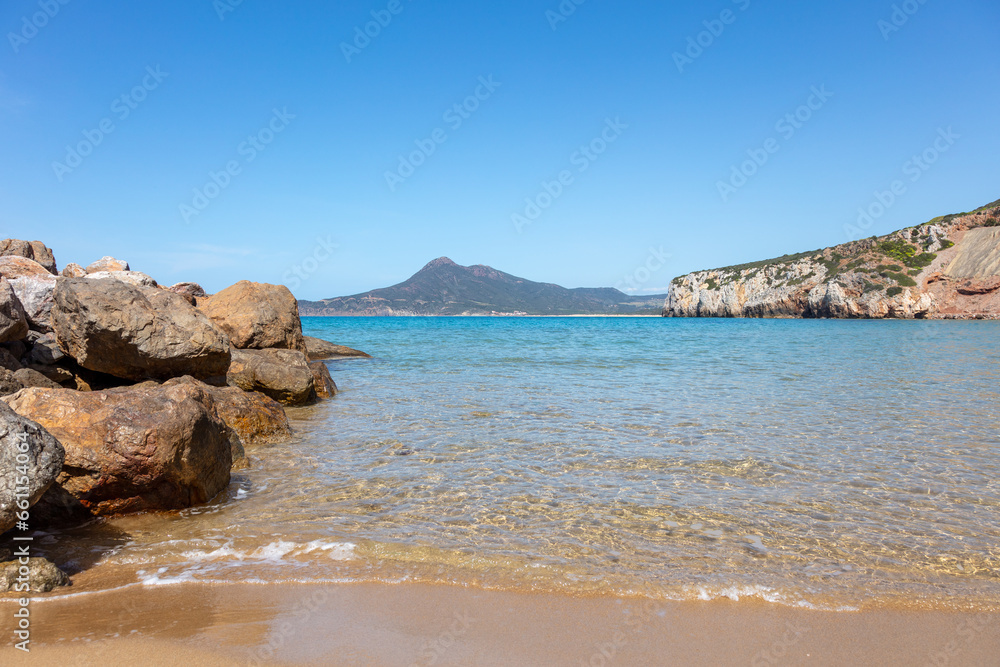 large boulders lying on the sea shore, clear water and mountains in the background