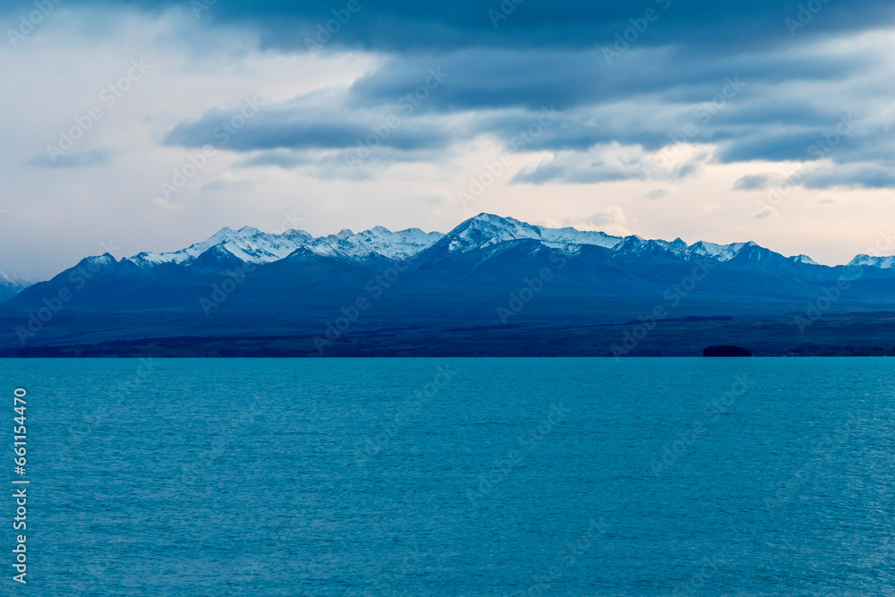 Photograph of Lake Pukaki early in the morning on a cloudy day with snow-capped mountains in the background on the South Island of New Zealand