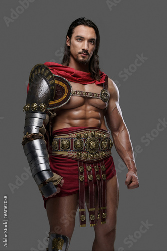 Majestic gladiator in sleek light armor and red cloak strikes a pose while holding a helmet against a gray background