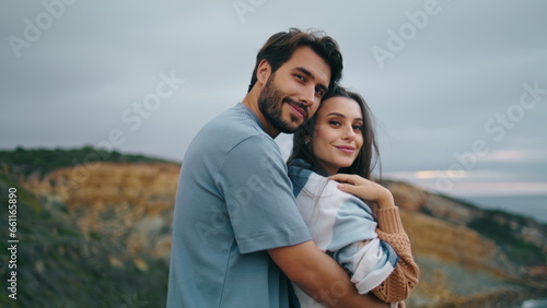Smiling pair looking camera standing hill top in front gray calm ocean close up.