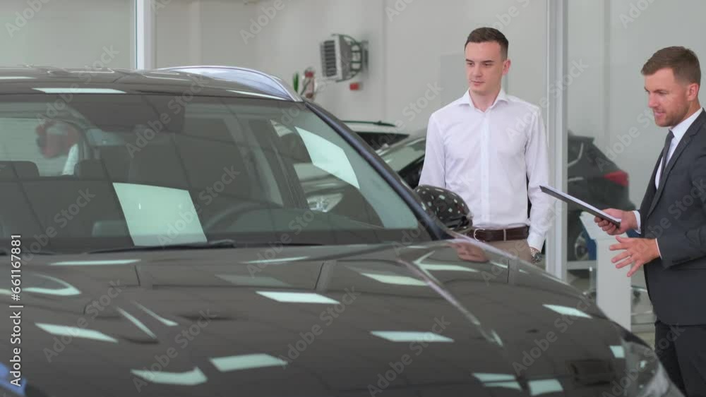 Young guy standing near nice black sports car, talking to dealer, side view. Young guy standing near nice black sports car, talking to dealer, side view.