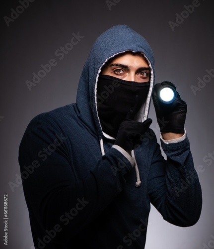 Young gangster in hood on grey background