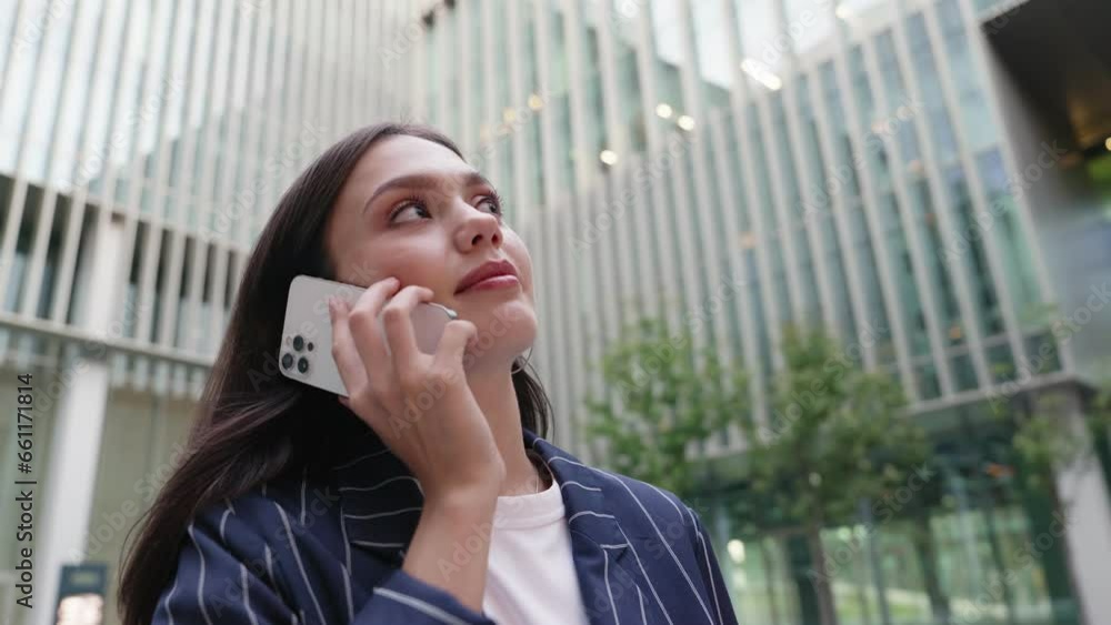 Low angle wide-angle shot of a young businesswoman in a suit having a phone conversation near a modern office building Low angle wide-angle shot of a young businesswoman in a suit having a phone conversation near a modern office building