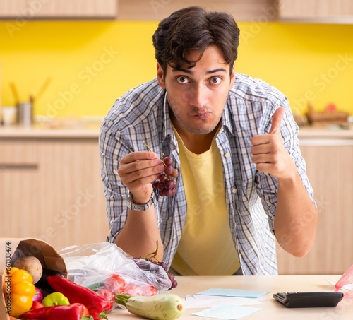 Young man calculating expences for vegetables in kitchen photo