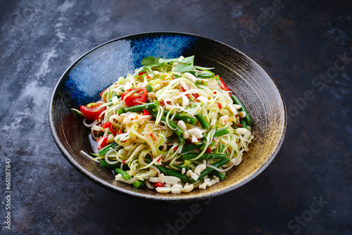 Traditional Thai green papaya som tam salad with green papaya slices, cherry tomatoes and beans in sweet sour fish sauce served as close-up on a Nordic design bowl