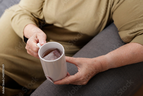 older woman hands with cup of tea on sofa