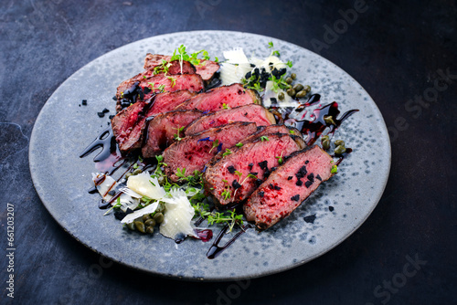 Italian tagliata de manzo roast beef steak slices with parmesan and capers served as close-up on a Nordic design plate with copy space
