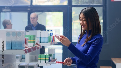 Joyful shopper in professional apothecary holding shopping basket, looking to buy prescription pills and other supplements. Happy asian client in drugstore looking for prescribed medication
