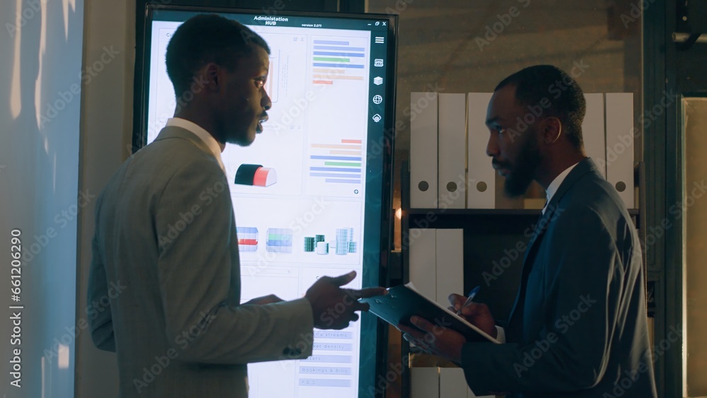 Manager looking at digital screen with employee, showing him researching key data needed for finding business insights and finishing project task. Company executives analyzing financial charts Manager looking at digital screen with employee, showing him researching key data needed for finding business insights and finishing project task. Company executives analyzing financial charts
