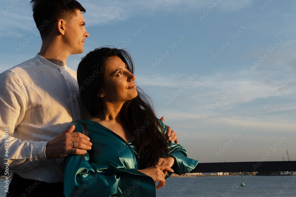 Young happy couple in love of different nationality hugging and kissing near river. Asian woman and european man.