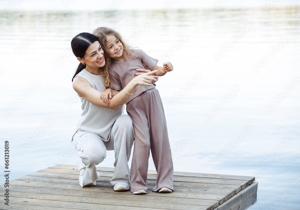 A young mother and her five-year-old daughter watch the fish in the lake, standing on the bridge.