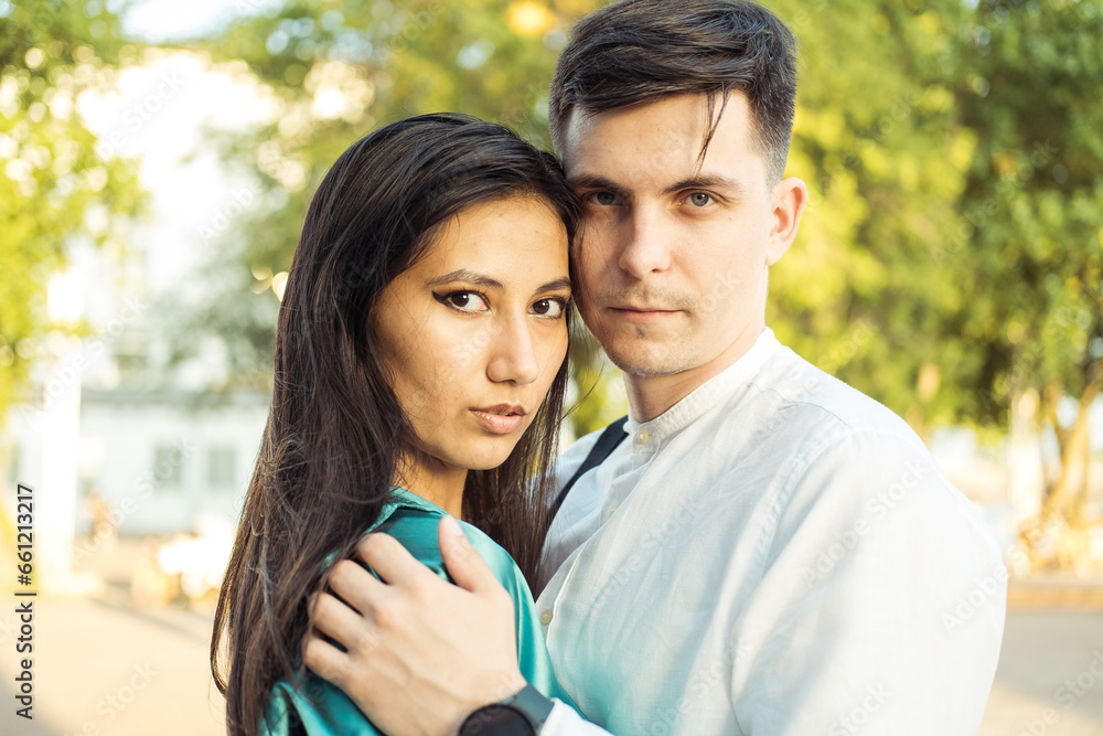 Young happy couple in love of different nationality hugging and kissing in the park. Asian woman and european man. Young happy couple in love of different nationality hugging and kissing in the park. Asian woman and european man.