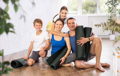 Happy family members sitting on the floor with black mats in hands in training room © JackF