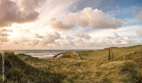 Picturesque coastal landscape on the Danish North Sea coast with the sunset and beautiful sky with soft clouds and sun rays. In the dunes near Blavand with strong winds and waves on the beach. Holiday