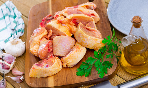 Fresh raw chopped chicken pieces on a wooden cutting board with a sprig of fresh parsley, garlic and vegetable oil during ..cooking in a home kitchen