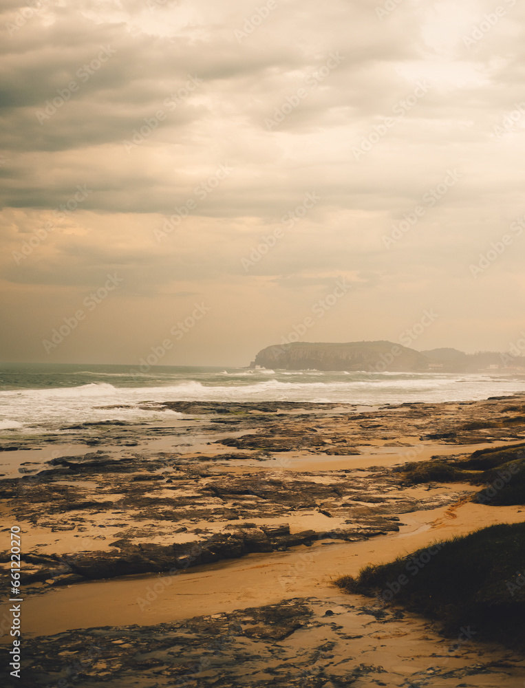 Brazilian beach on evening. Cloudy sky with hills in the background and rocks in the sand. Rough seas. Torres - Brazil