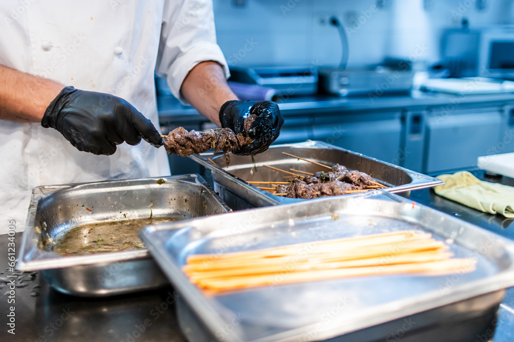 The hands of a chef with black gloves preparing veal skewers for the restaurant service The hands of a chef with black gloves preparing veal skewers for the restaurant service