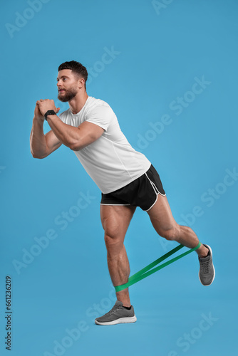 Young man exercising with elastic resistance band on light blue background