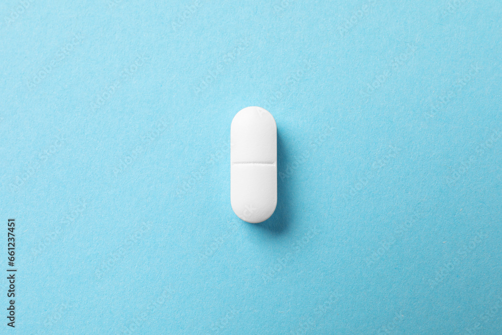 One white pill on light blue background, top view One white pill on light blue background, top view