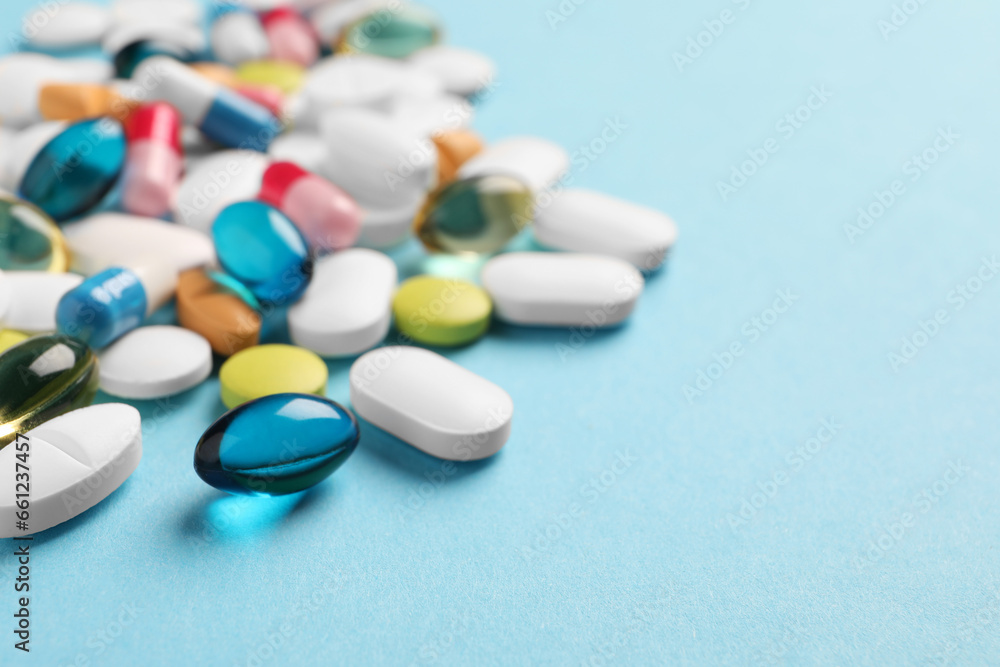 Pile of different pills on light blue background, selective focus. Space for text Pile of different pills on light blue background, selective focus. Space for text