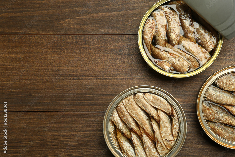 Open tin cans of sprats on wooden table, flat lay. Space for text Open tin cans of sprats on wooden table, flat lay. Space for text