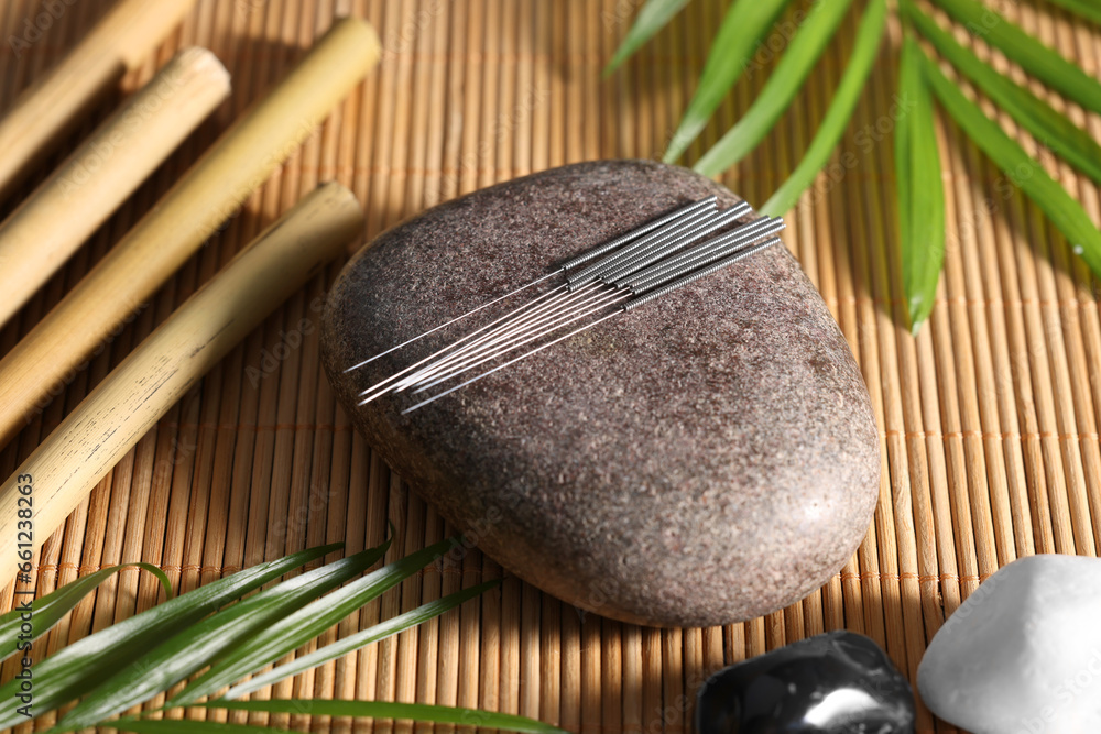 Stone with acupuncture needles on bamboo mat, above view - obrazy, fototapety, plakaty 