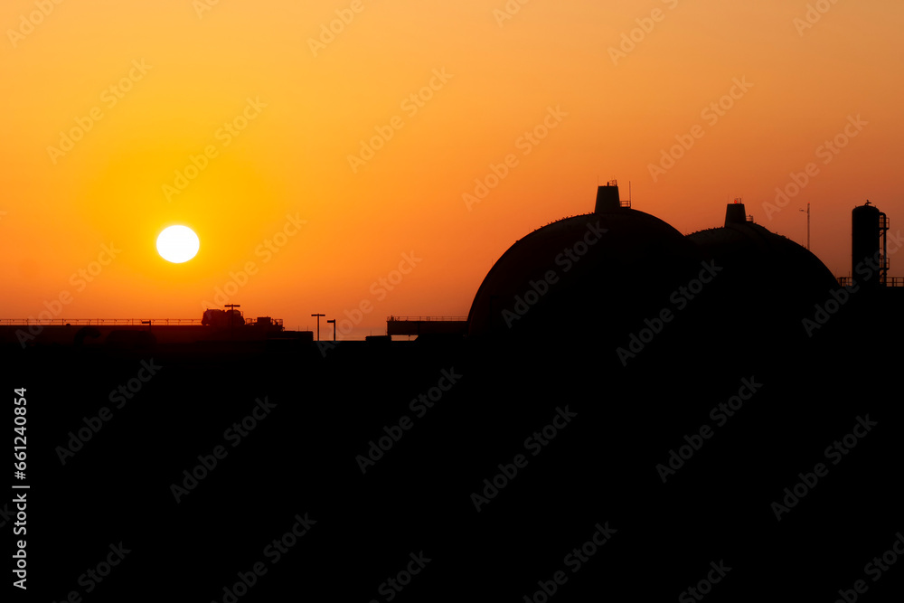 Silhouette of San Onofre nuclear power plant main reactors at sunset with sun visible.