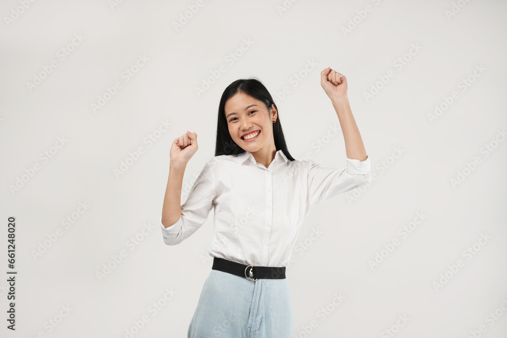 Happy young Asian woman raising his fists doing yes gesture, isolated on soft grey background. Happy young Asian woman raising his fists doing yes gesture, isolated on soft grey background.