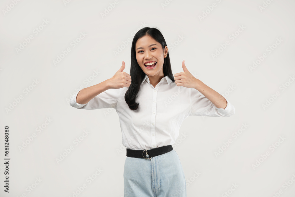 Photo of a young Asian girl wearing casual white clothes smiling and doing thumb up, and approval sign. Photo of a young Asian girl wearing casual white clothes smiling and doing thumb up, and approval sign.