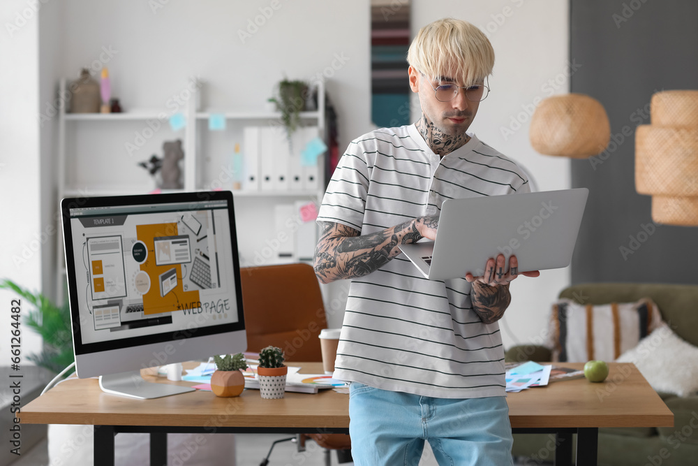 Tattooed graphic designer working with laptop in office - obrazy, fototapety, plakaty 