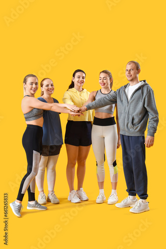 Group of sporty young people putting hands together on yellow background