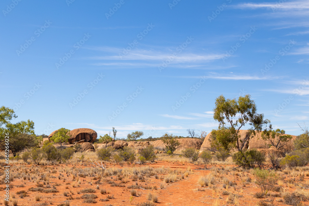 Granite boulders surrounded by drought resistant trees, bushes and grasses in a semi arid environment with blue sky background in Queensland, Australia.
