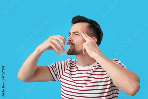 Young man drinking water with dissolved tablet on blue background