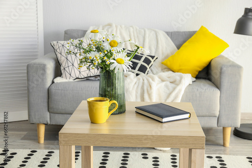 Interior of stylish living room and vase with blooming chamomile flowers on wooden table © Pixel-Shot