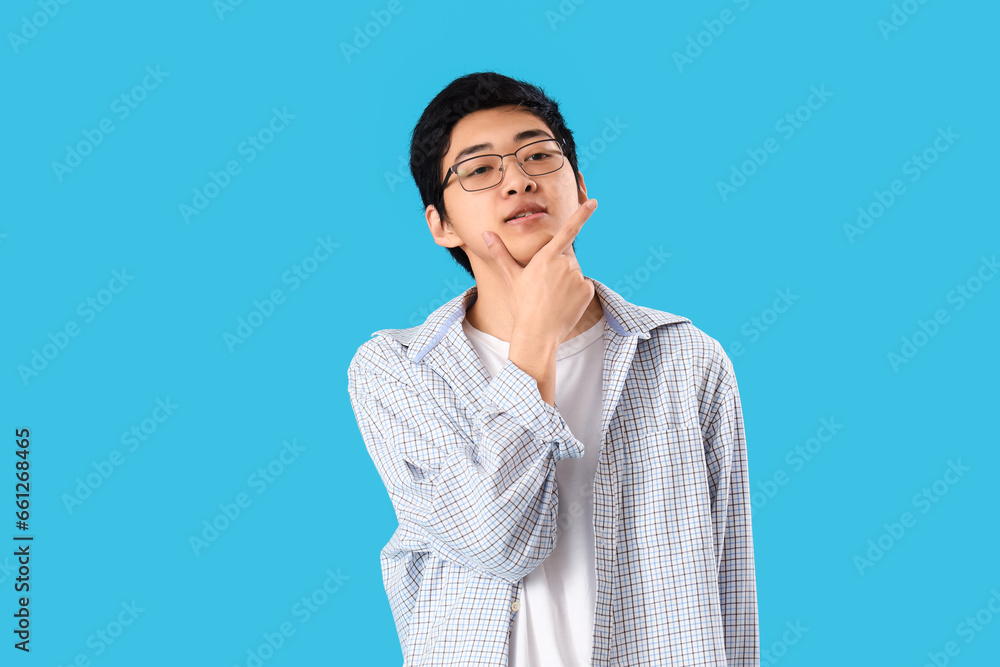 Thoughtful young Asian man on blue background Thoughtful young Asian man on blue background
