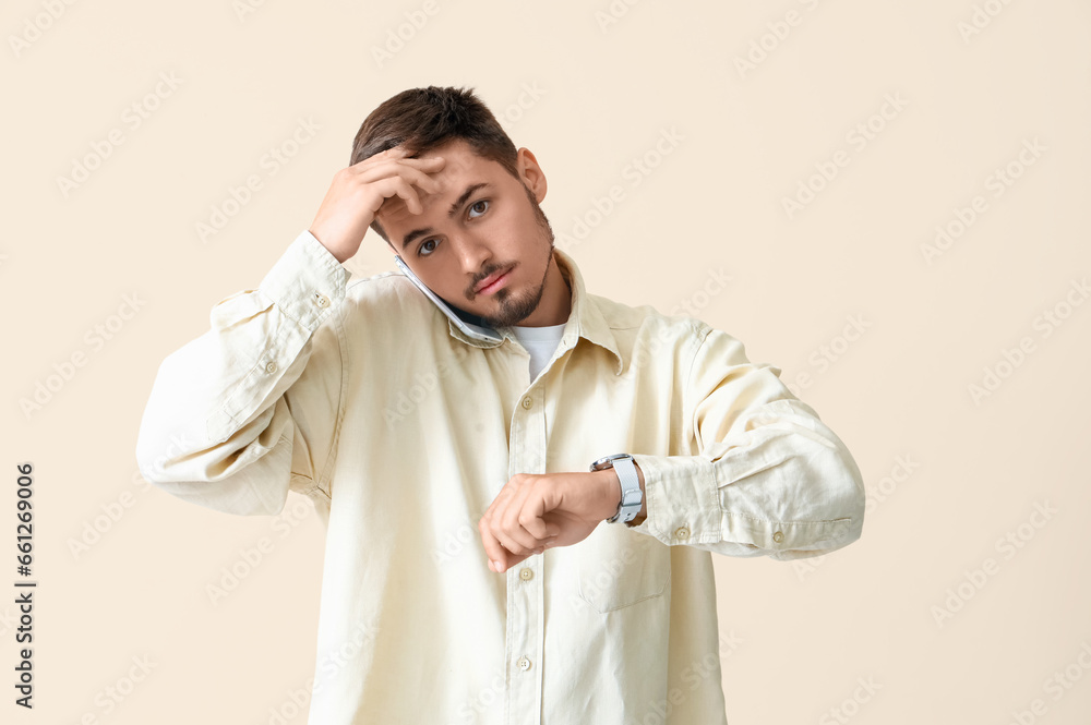 Stressed young man looking at wristwatch on beige background. Deadline concept Stressed young man looking at wristwatch on beige background. Deadline concept