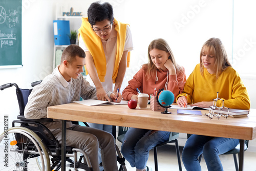 Group of teenage students with boy in wheelchair studying at school